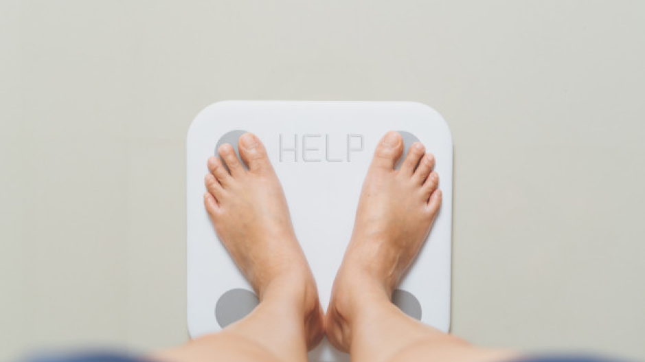Overweight female is standing on white scales at home with help word Premium Photo