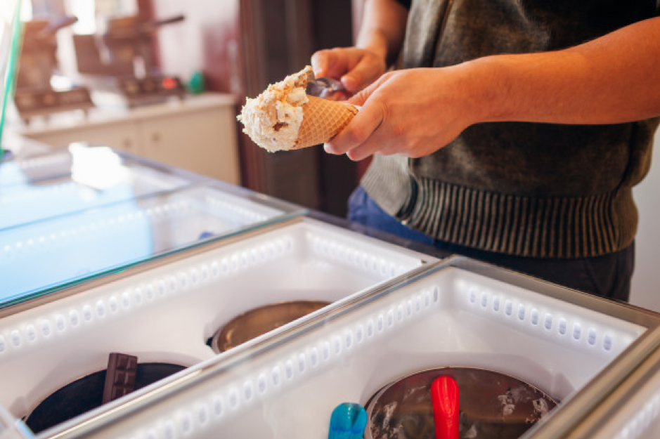 Seller filling waffle cone with ice-cream. vanilla flavour with cookies crumbs Premium Photo